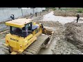 Huge SHANTUI Dozer working with dirt & mud to block the water use soil process with big dump trucks